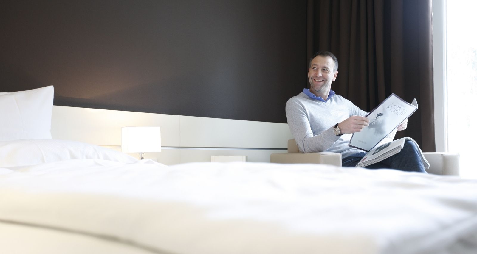 Ein Mann der Zeitung liest und auf dem Bett sitzt 