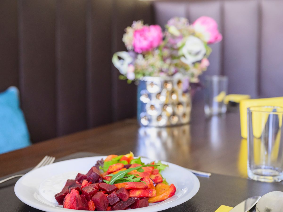 Teller mit buntem Gemüse daneben steht ein Blumenstrauß mit Rosen