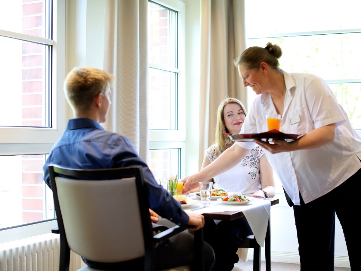 Zwei Personen sitzen im Restaurant und eine Frau serviert das Essen