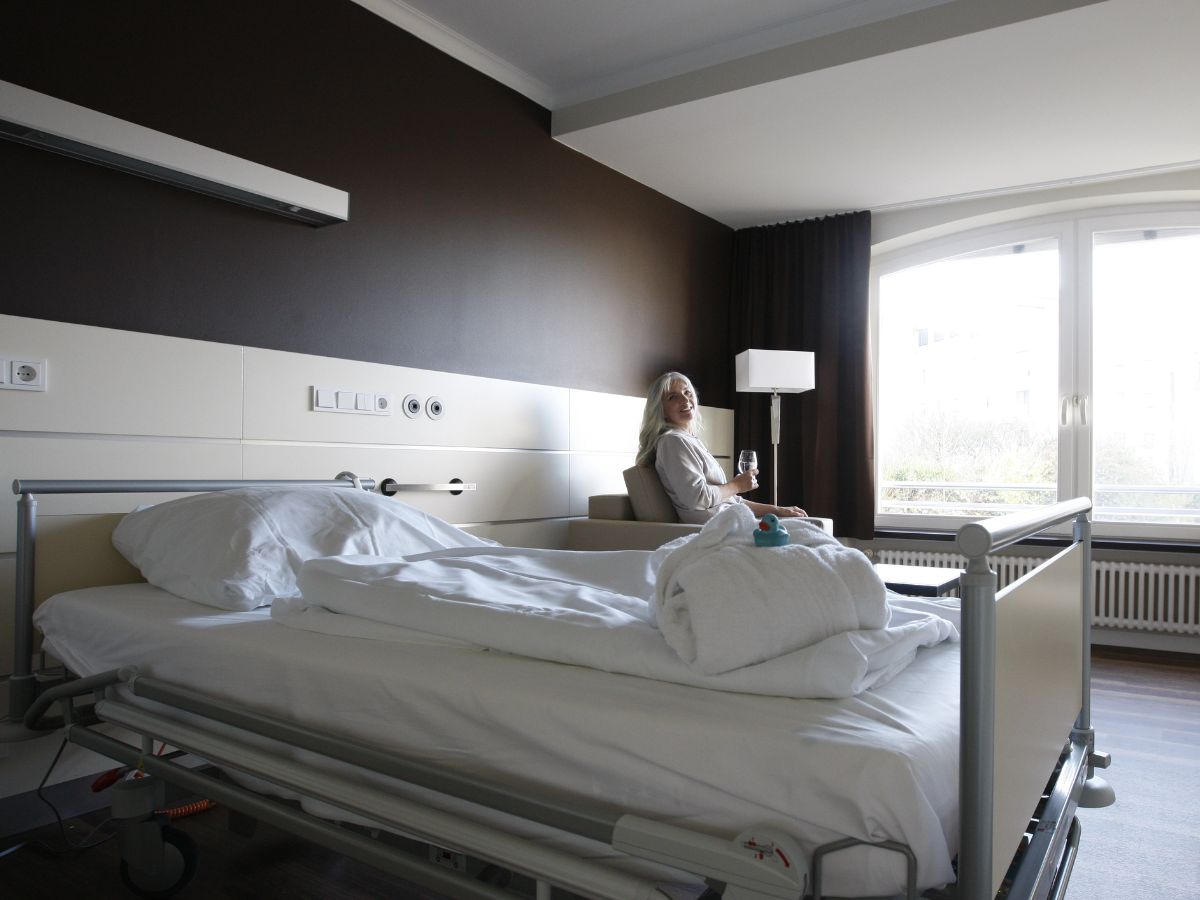 Komfort Zimmer mit Einzelbett und im Hintergrund Frau auf einem Sessel